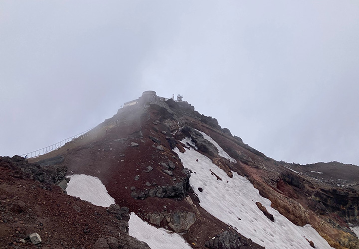 写真1. 残雪が見られる7月初旬の富士山頂。建物は富士山特別地域気象観測所（旧富士山測候所）。